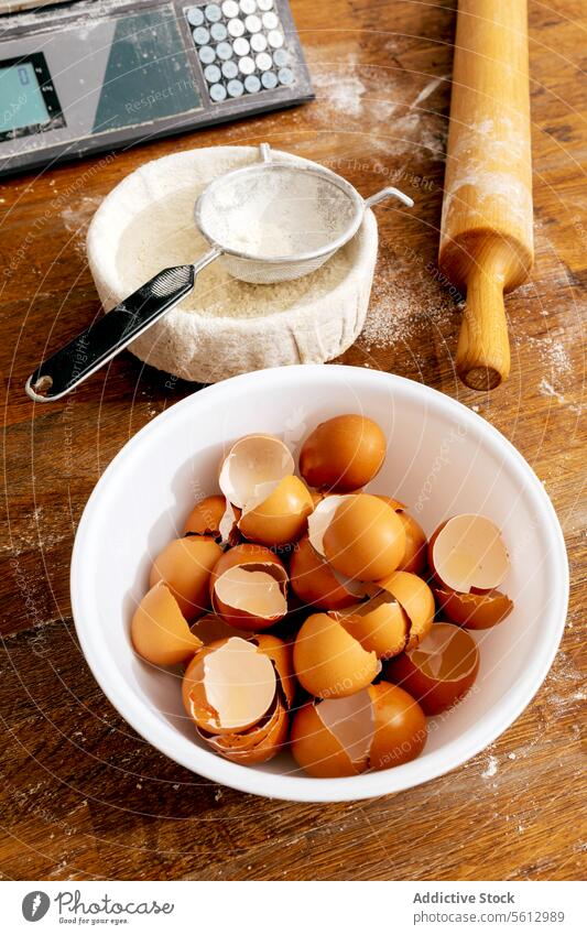 Flour and eggshells with utensils on table in bakery flour sieve rolling pin bowl wooden making pastry food bakehouse high angle tool fresh kitchen cooking