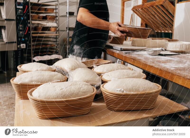 Man covering bread dough in container with plastic male baker sourdough mold table bakehouse focus professional uncooked raw wooden concentrate kitchen bakery