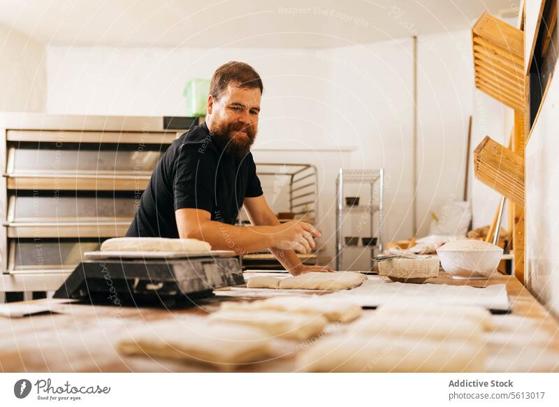 Cook preparing dough on table in bakery kneading pastry bakehouse kitchen focus beard casual attire occupation business food cook prepare chef cookery making
