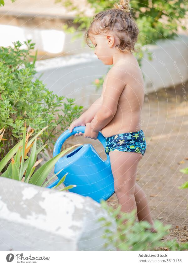 Side view of shirtless little boy watering fresh plants with can in garden during vacation green summer sunny nature growth backyard gardening lifestyle