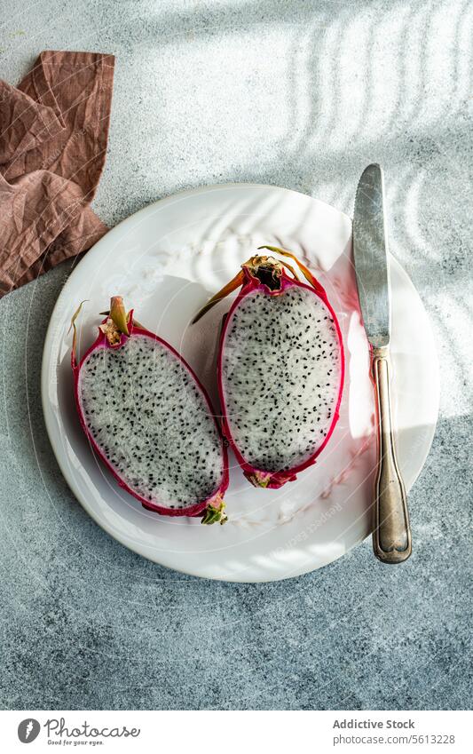 Fresh dragonfruit halves on a white plate with knife shadow texture table vintage silverware fresh cut vibrant tropical stylish healthy exotic marble food