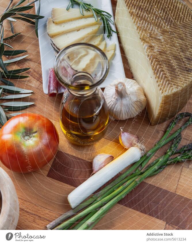 Artisan cheese and fresh ingredients on a wooden board artisan olive oil tomato asparagus garlic onion cutting board culinary food cuisine mediterranean kitchen
