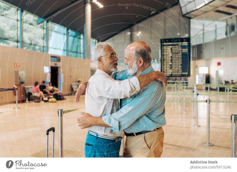 Senior travelers hugging at modern airport friends embrace happy luggage side view farewell aerodrome together stand suitcase casual attire separation departure