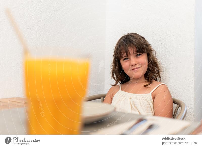 Calm girl with drink sitting on chair in cafe portrait smiling cute wall casual attire lifestyle leisure white looking at camera kid child table restaurant