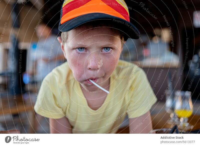 Serious child eating lollipop in cafe boy portrait serious cap caucasian innocent person lifestyle kid childhood elementary little blurred background