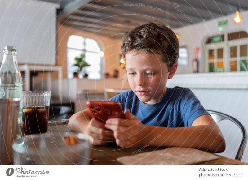 Boy playing on smart phone in restaurant boy using smartphone innocent cafe dining table sitting person lifestyle kid childhood mobile internet digital online