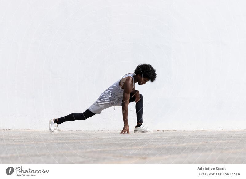 Side view of concentrated black male athlete in sportswear and sneakers stretching body while bending on street during fitness workout in city man exercise