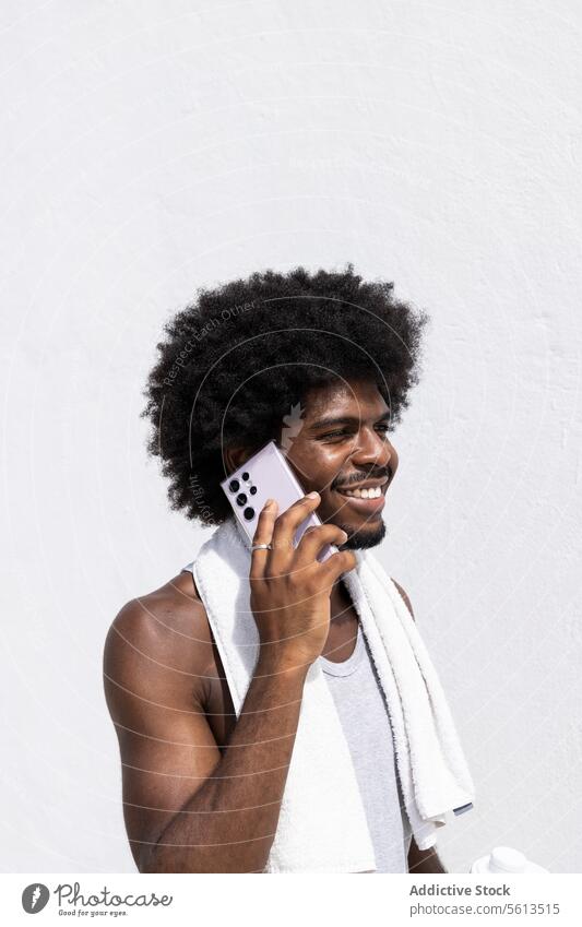 Male athlete on phone call over white background man exercise afro hair smile mobile talk sportsman towel looking away communication active wall happy speak