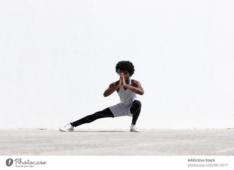 Serious black sportsman exercising over white wall athlete exercise afro hair prayer pose stretch leg squat balance street stamina effort anonymous half face