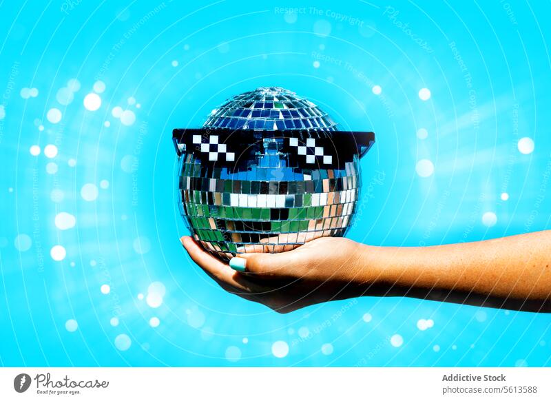 Woman with party glasses on disco ball against blue background hand woman holding illuminated bright glow lens flare anonymous trend club shiny trendy faceless