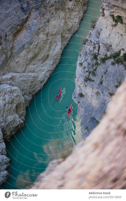 High angle view of unrecognizable people kayaking on blue narrow river flowing between rocky mountains during vacation at daytime from above boat transport