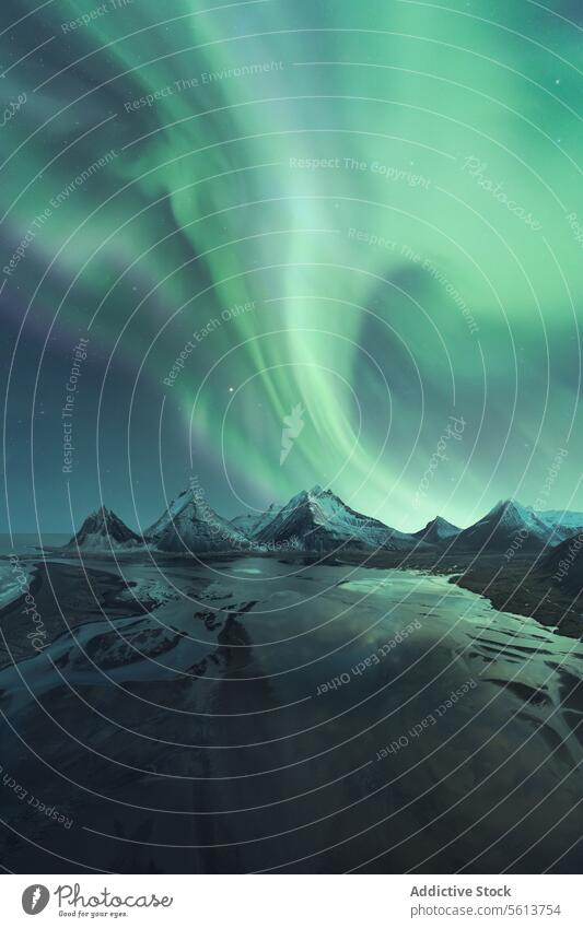 Spectacular northern lights over snow-covered mountains in Iceland aurora borealis night sky natural spectacle landscape phenomenon arctic cold winter green