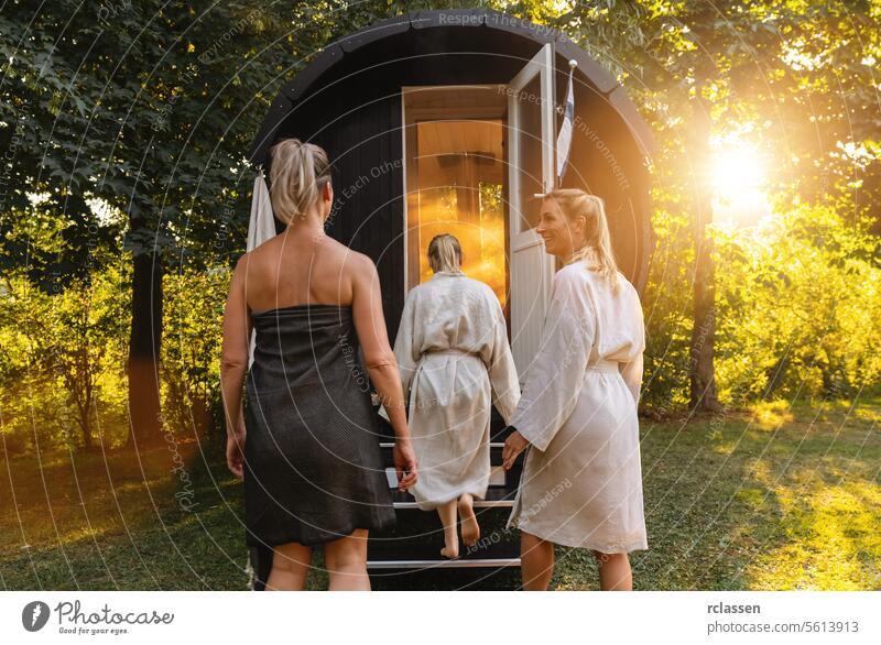 Three people in robes goes in a Finnish sauna barrel in a sunlit forest at sunset woman happy people wood barrel mobile finnish sauna sauna cabin relaxation