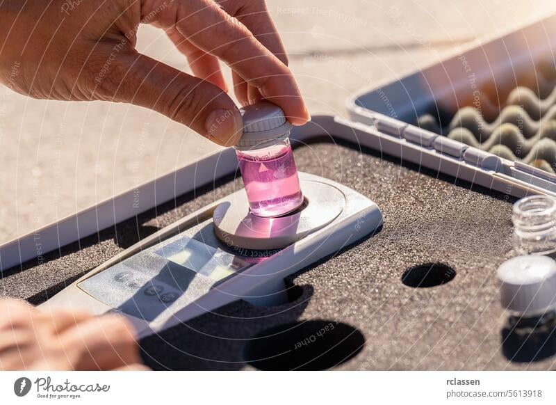 Hand placing a pink liquid bottle on a digital analysis device in a testing kit chemical analysis laboratory water quality ph testing kit solvent dispensing