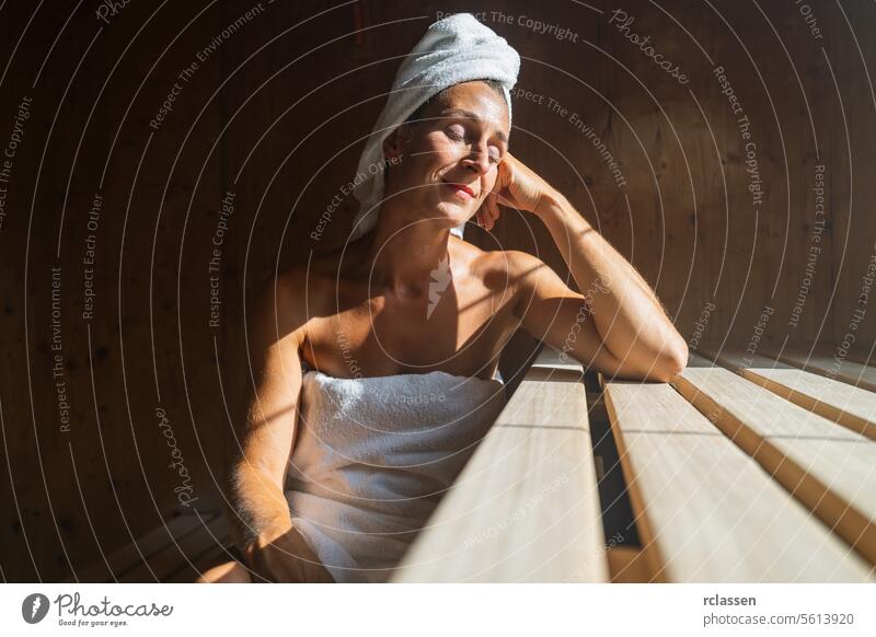 Woman in a finnish sauna leaning back, eyes closed, with a towel wrapped around her head, sunlit at a spa resort vihta wellness spa hotel window sweat finland