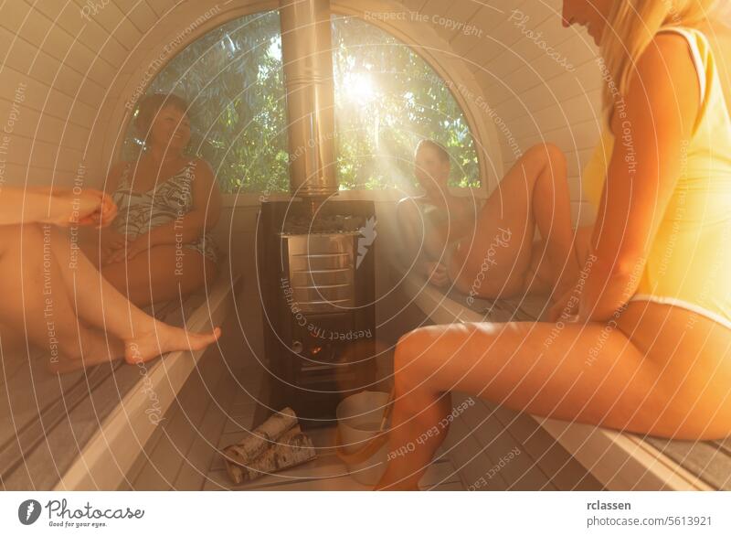 Three women enjoying a sauna session, sunbeam through window, stove with firewood relaxation wellness health spa heat wood stove friendship leisure self-care