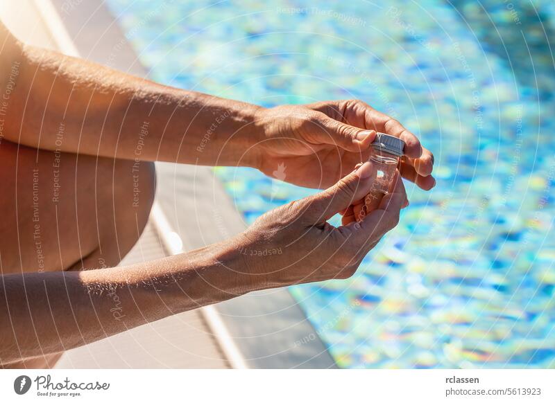 Hands closing a small vial of water for pH testing near a pool with sunlight reflecting on the surface ink liquid yellow liquid value chlorine measure sample