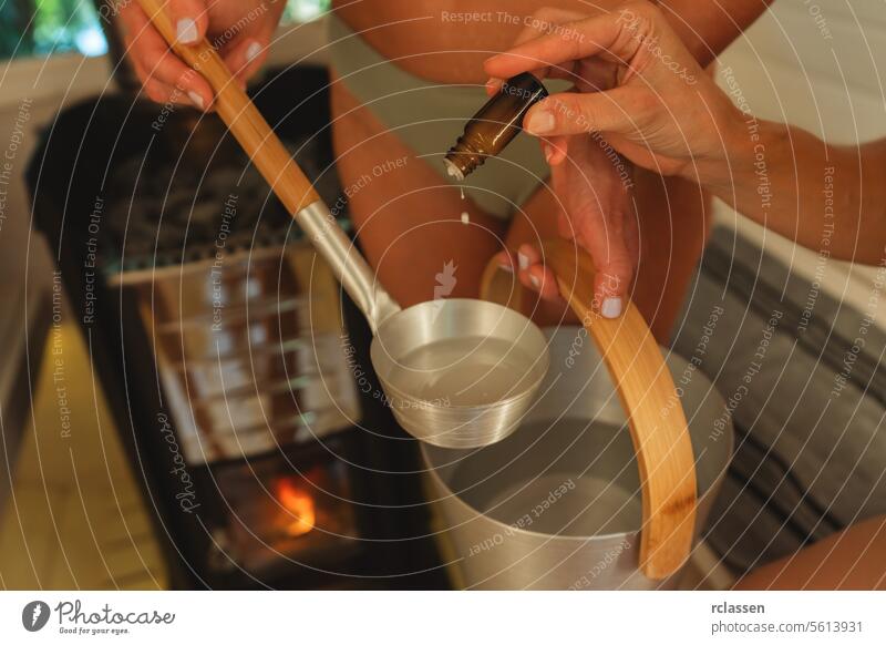 Close-up of hands pouring essential oil into a sauna ladle over a bucket. Finnish mobile sauna concept image aroma aroma therapy bathing suits calm care comfort