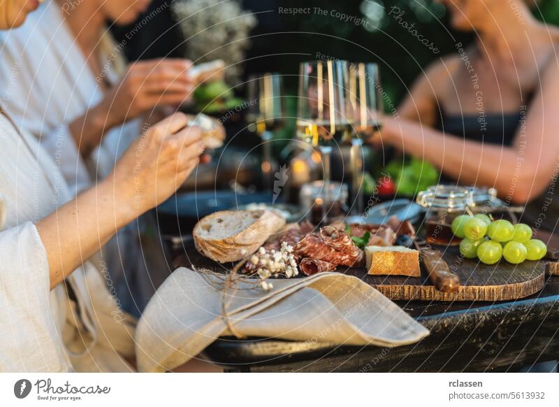 Close-up of a table with wine glasses, bread, and grapes, friends dining in the background close-up charcuterie outdoor dining evening cheese meal leisure