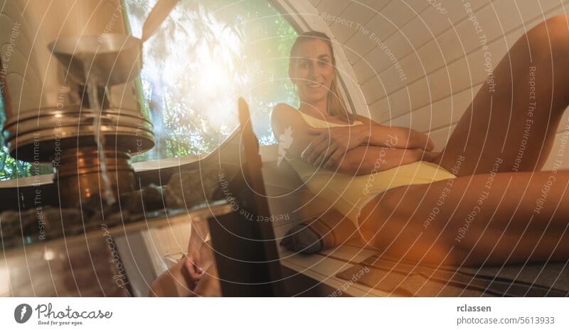 Relaxed woman sitting in a sauna, water being poured on hot stones in the foreground. Mobile finish sauna concept image pouring water relaxation wellness