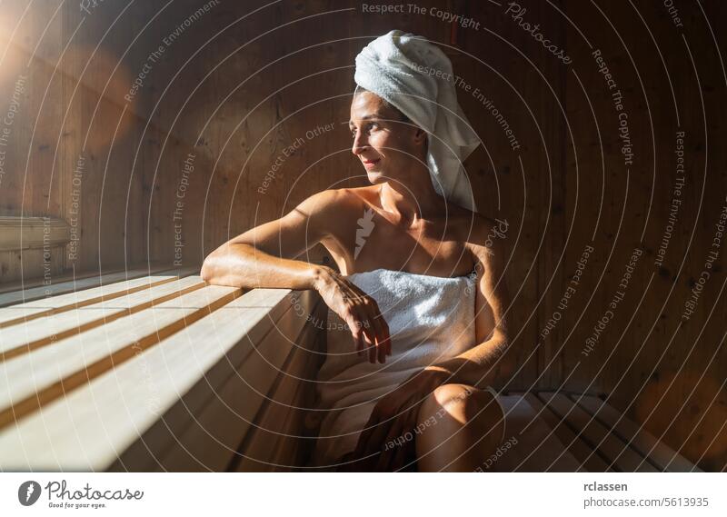 Woman sitting in a finnish sauna, leaning on one arm, with a towel wrapped around her head, sunlight streaming in at wellness spa hotel vihta resort window