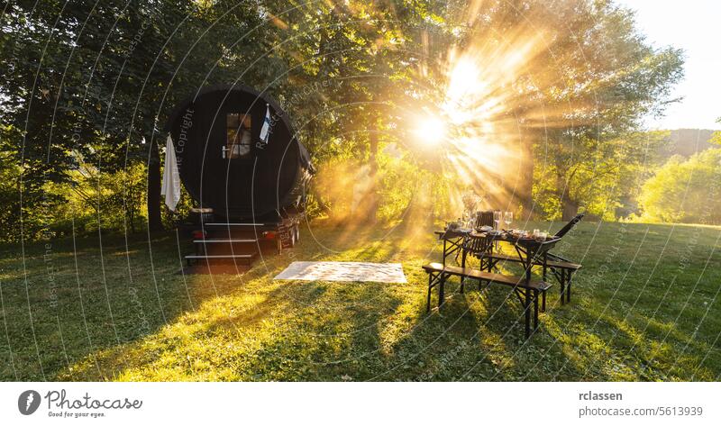 Sun rays shining over a Finnish mobiel sauna barrel and a set table in a lush meadow resort hotel flag sunrays appetizer wine wooden barrel fresh food