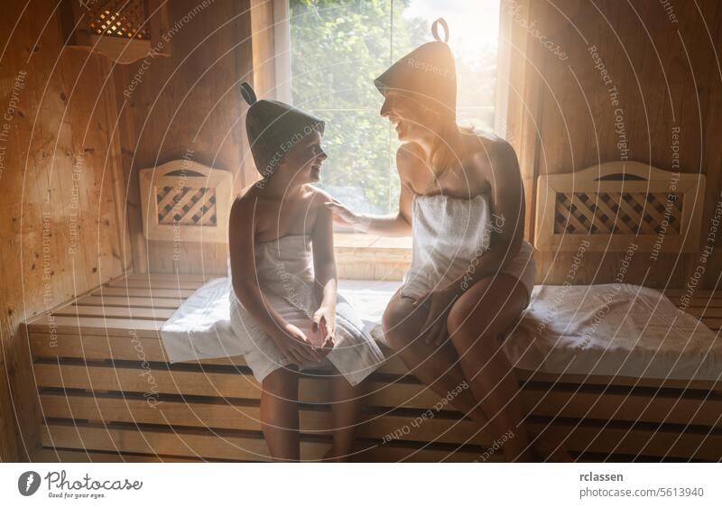 Mother and daughter enjoying a sauna session, wearing felt hats and wrapped in towels bathrobe steam spa wellness hotel calm family woman smiling relaxation