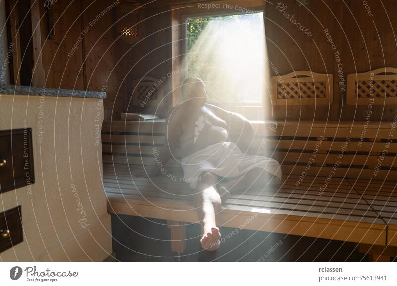 Man sitting in a sauna with light streaming through the window onto his relaxed figure. wellness spa resort hotel sweat finland finnish man in sauna smiling