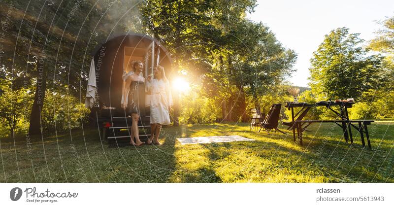 Two people exiting a Finnish sauna barrel in a forest at sunrise with a picnic table nearby. woman happy people wood barrel fog mobile finnish sauna sauna cabin
