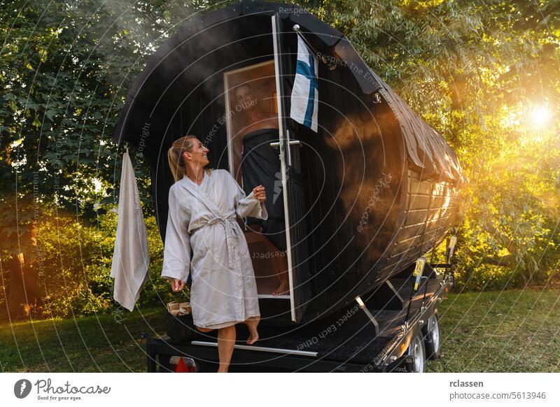 People in bathrobes standing in front of a mobile Finnish sauna barrel with steam around them fog finnish sauna sauna cabin relaxation wellness nature people