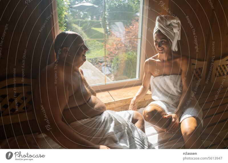 Man and woman in a sauna, woman with a towel on her head, both smiling and sitting at spa wellness hotel wellness spa resort window sweat finland finnish