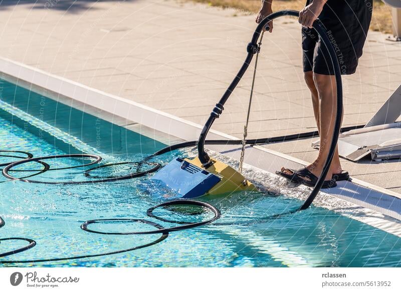 Person operating a pool vacuum cleaner at the side of a swimming pool woman service industry technician uniform robotic cleaner pool care summer pool equipment