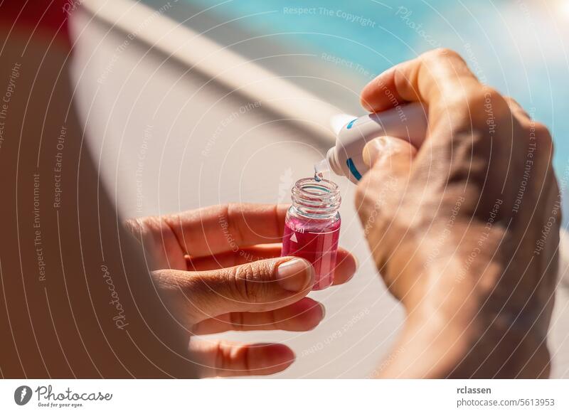 Hands of a pool technician dispensing with dropper bottle solvent into a vial with pink solution  for pH testing ink liquid yellow liquid value chlorine measure