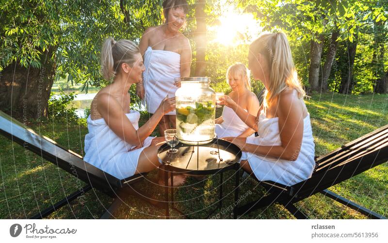 Group of women in white towels enjoying infused water with lemons in a park after  finnish sauna mint lime group of women enjoyment relaxation spa wellness
