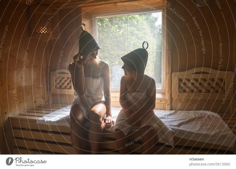 Mother and daughter in a sauna, both wearing felt hats, enjoying a conversation in a spa hotel bathrobe steam spa wellness calm family woman smiling relaxation