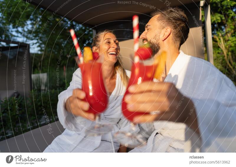 Couple in white robes toasting with red cocktails outdoors at spa resort bathrobe wellness hotel spa wellness resort couple joyful relaxation leisure luxury
