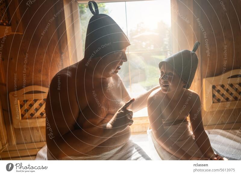 Father and daughter in finnish sauna, wearing felt hats, father talking and daughter listening. hotel pointing sweat wooden bench warmth wellness health steam