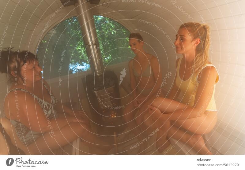 Four women sitting in a Finnish barrel sauna, smiling and enjoying the heat mobile steam hot stones relaxation wellness bathing suits wooden interior