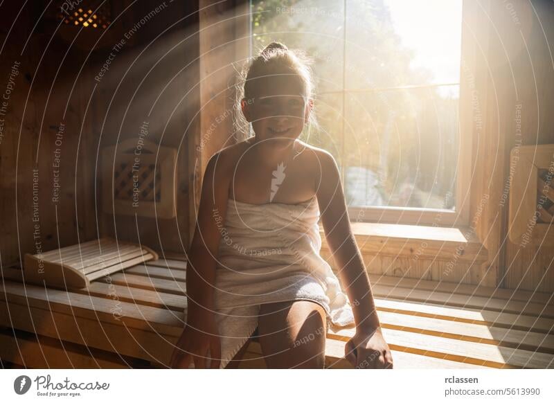 Smiling child in a finnish sauna, sun rays beaming through the window, wrapped in a towel at spa wellness hotel bathrobe beauty spa calm comfortable enjoy sweat