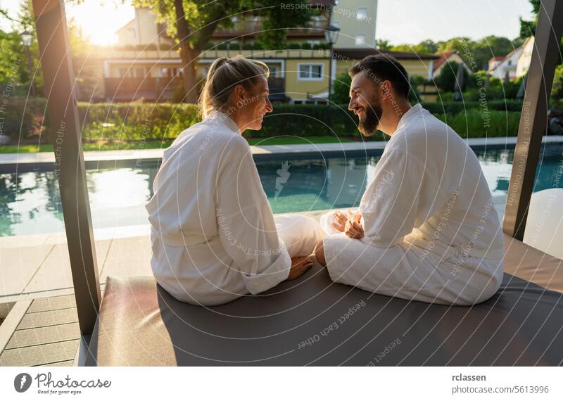 Couple in white bathrobes enjoying sunset by sitting by a pool in a spa wellness hotel resort love white robes couple relaxation leisure enjoyment outdoors