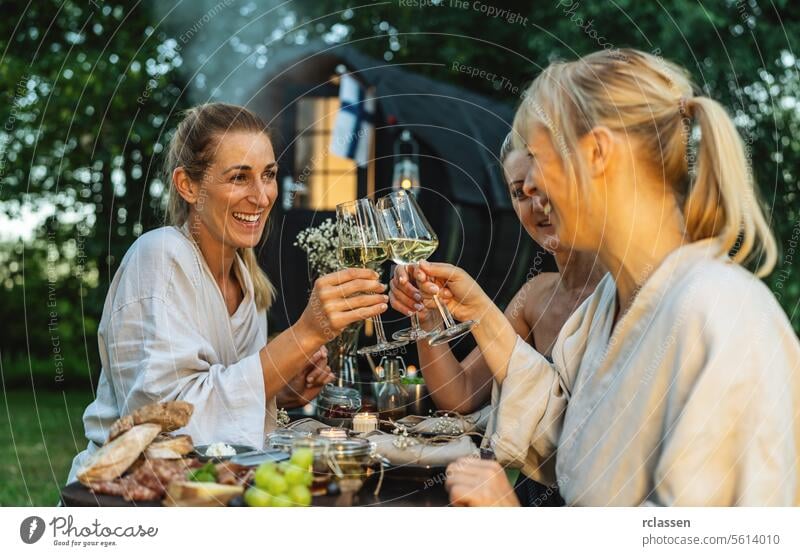 People in bathrobes toasting with wine glasses near a Finnish mobile sauna barrel outdoors woman beverages hot finnish sauna people relaxation celebration