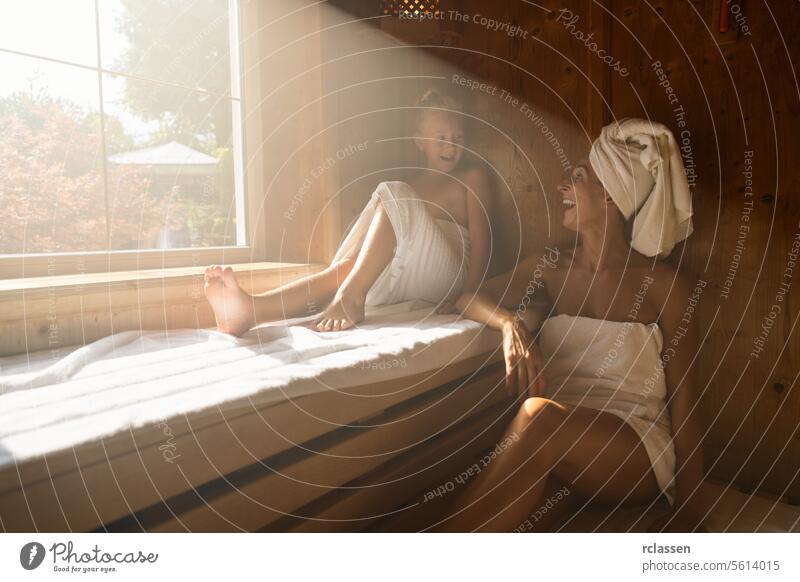 Mother and daughter in a sauna, mother with a towel on her head, both smiling and sitting child family wellness spa resort hotel window sweat finland finnish