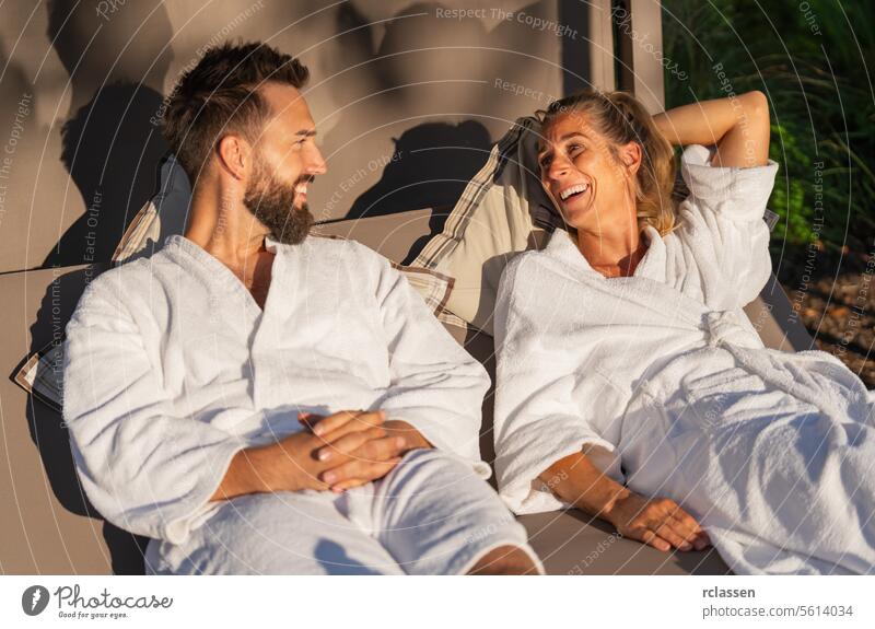 Couple in white robes reclining and enjoying a laugh on a lounger in the sunlight at a spa hotel bench lounger relax resort love wellness spa couple lounging