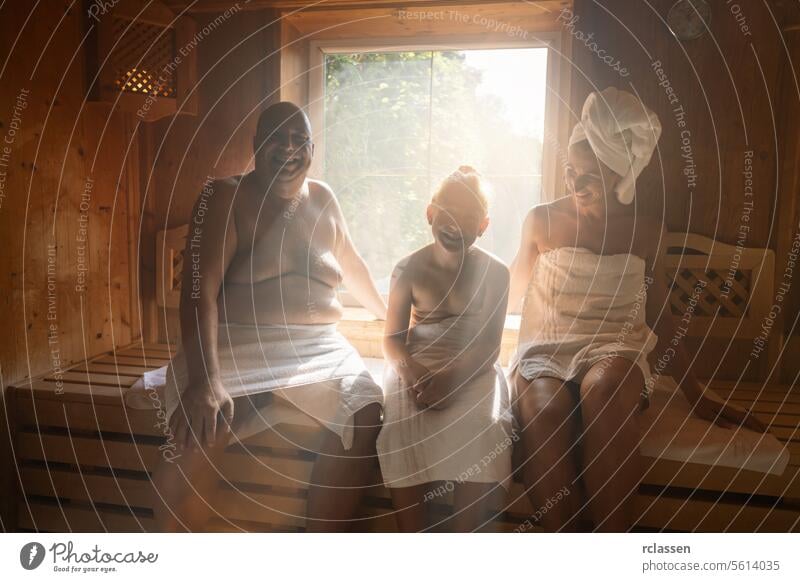 Family in a finnish sauna laughing together, man on left, woman with towel on head on right, child in middle at wellness hotel finland spa wellness family