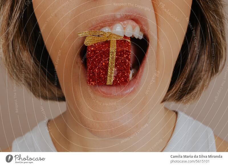 Close up of a female mouth biting a gift-shaped Christmas ornament. attitude beautiful beauty bright christmas ornaments closeup color concept detail eat