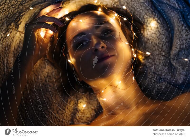 Close-up of a woman's face with fairy lights string Illuminated Tangled Night Dark Lying Down Head Evening electric Short Hair Tenderness sensuality relaxation