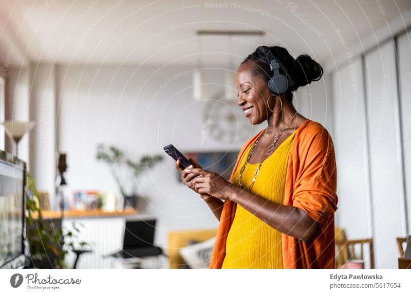 Woman listening to music with headphones connected to her smartphone in the living room at home people joy woman black natural attractive black woman happiness