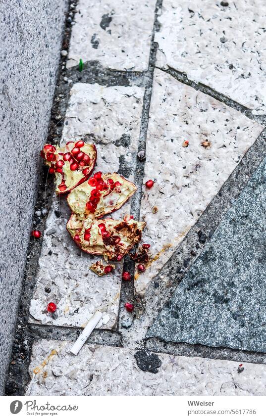 A broken pomegranate lies in the dirt next to a cigarette butt on the street Pomegranate Trash abundance Street Asphalt Dirty To fall Sludgy food luxury