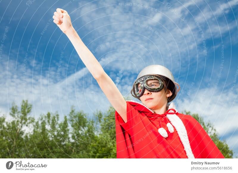 Low angle view of cute teen boy wearing metal cauldron as a helmet goggles and red costume - a funny power super hero child concept Superhero aspirations cape