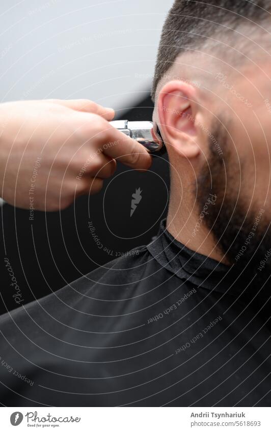 Barber shaves the temple with cordless trimmer during a short haircut on the sides of the head. razor man electric shaving bald handsome barber grooming male